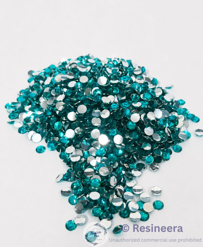 Firoji flatback rhinestones are scattered on fabric backgrounds with green leaves nearby.