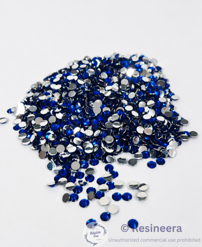 Blue flatback rhinestones are scattered on fabric backgrounds with green leaves nearby.